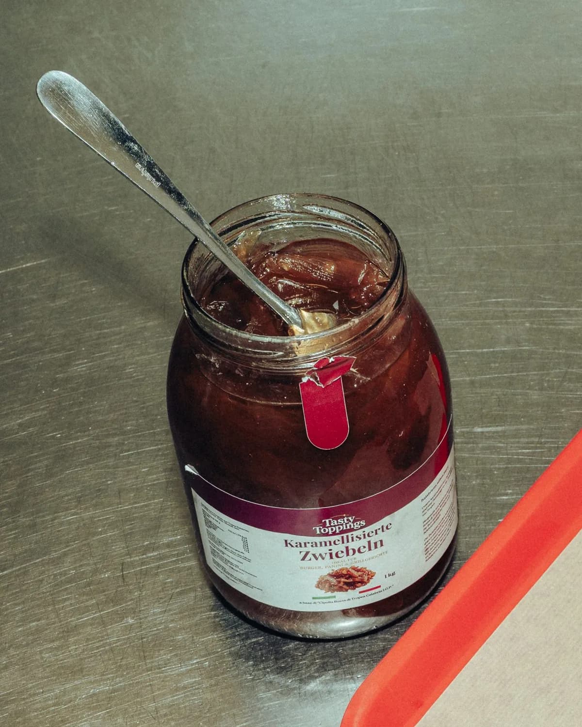 Geöffnetes 1-kg-Glas Tasty Toppings mit Löffel auf der Edelstahl-Arbeitsfläche